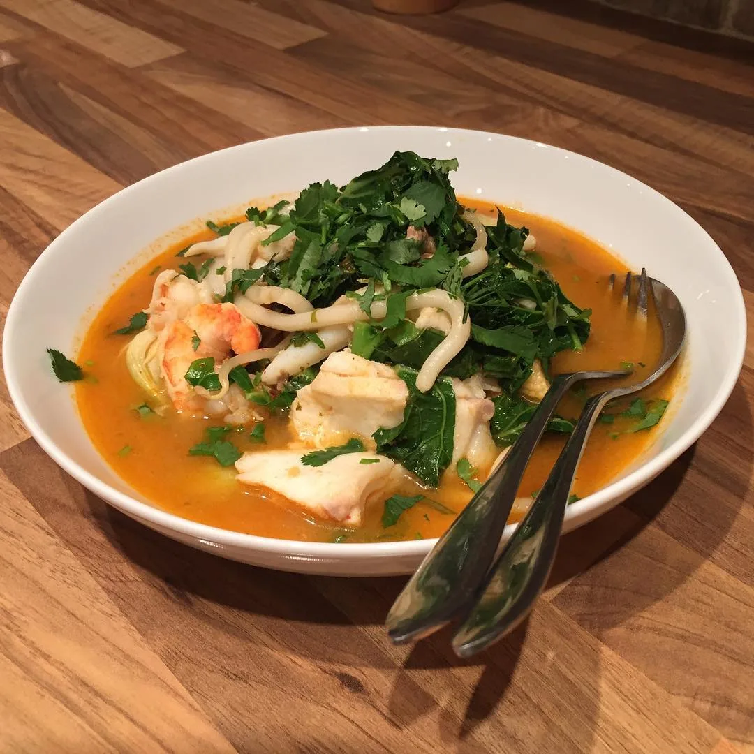 A bowl of broth with fish and fresh herbs